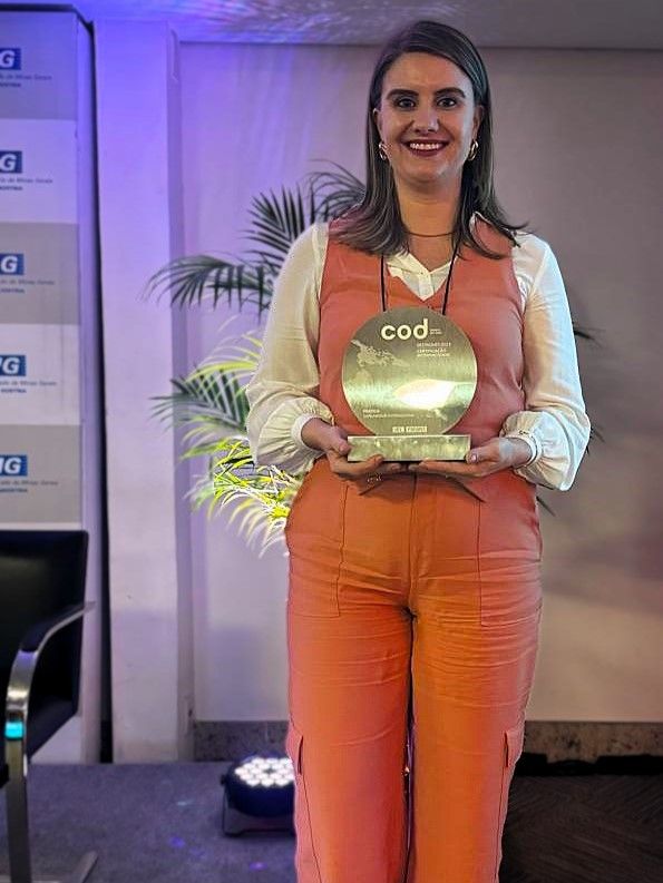 Uma mulher de calça laranja segura um troféu nas mãos.