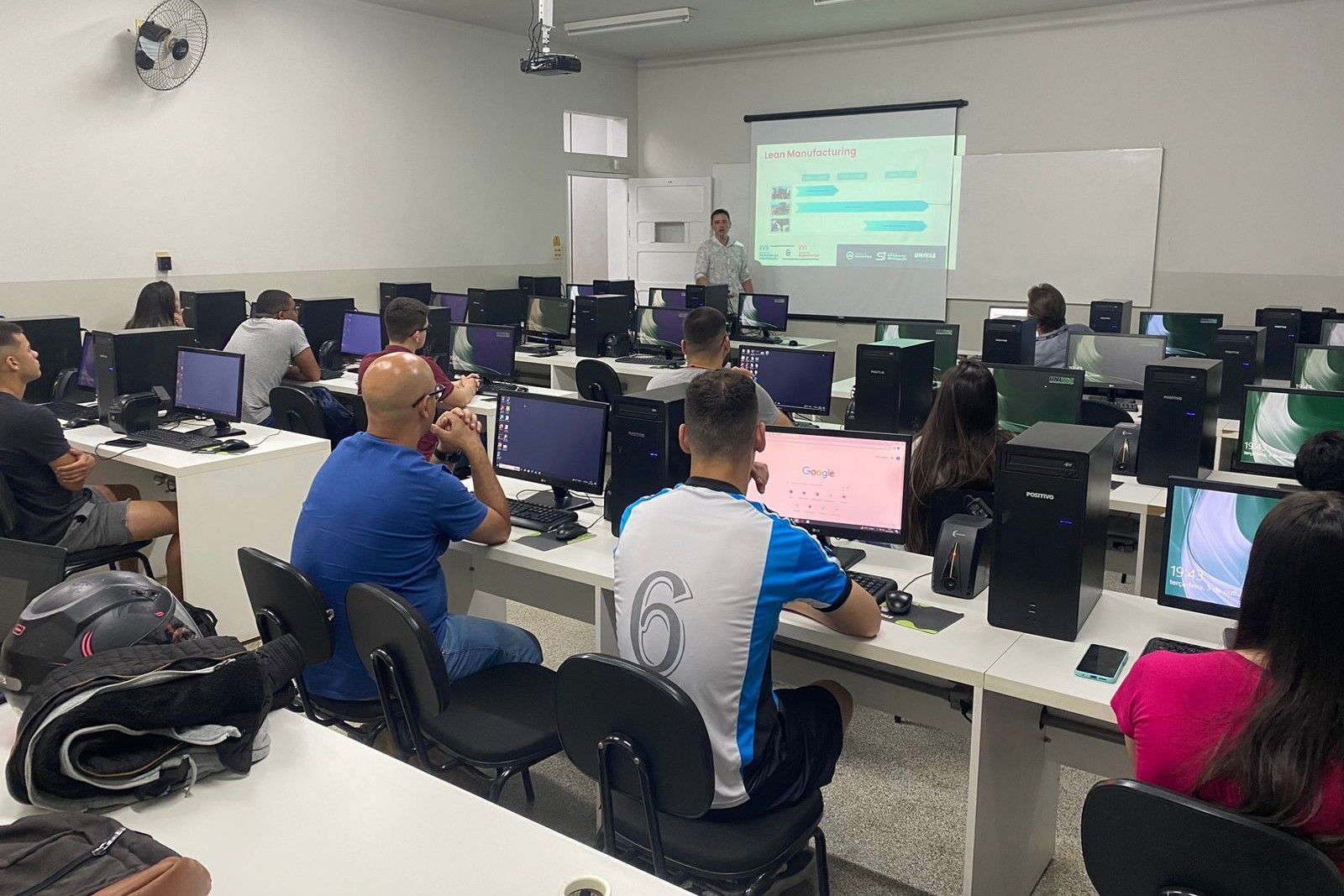 Um grupo de pessoas está sentado em mesas em um laboratório de informática.