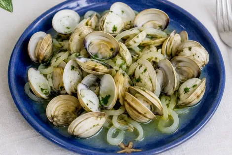 Prato azul de mariscos lambreta cozidas no vapor com ervas em caldo leve.