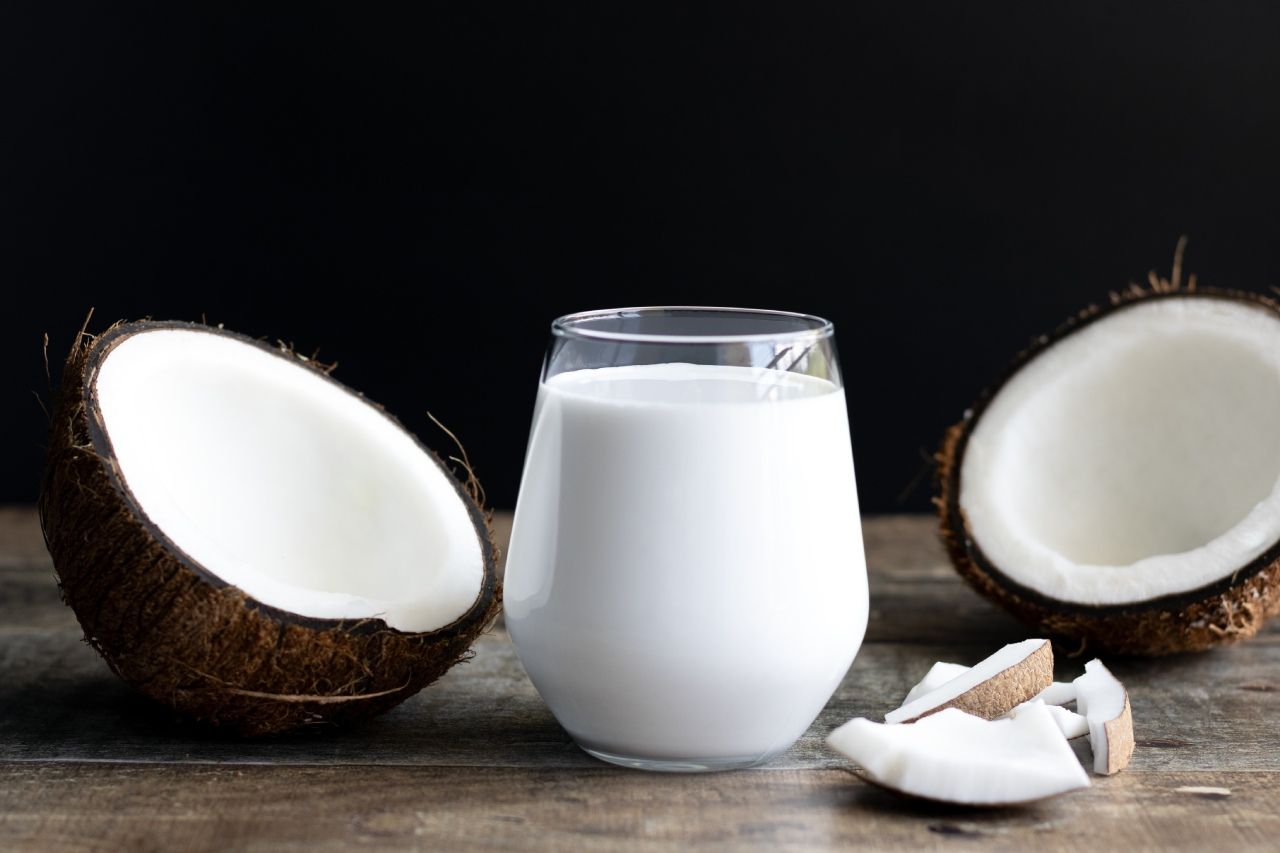 Leite de coco em um copo com metades de coco sobre uma superfície de madeira.