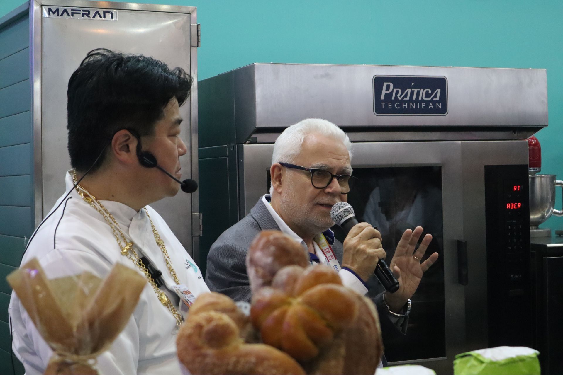 Dois homens estão de pé, um ao lado do outro, em frente a um forno.