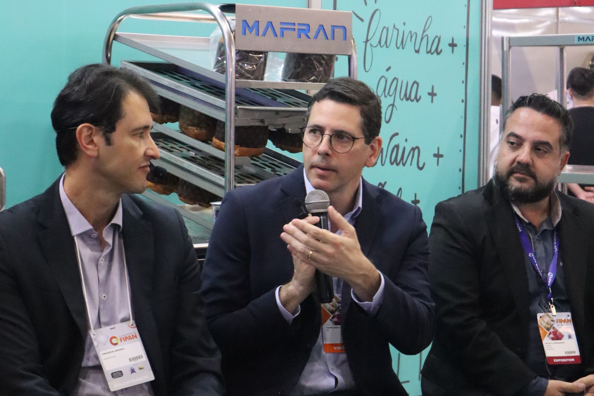 Três homens estão sentados em frente a uma placa que diz mafran