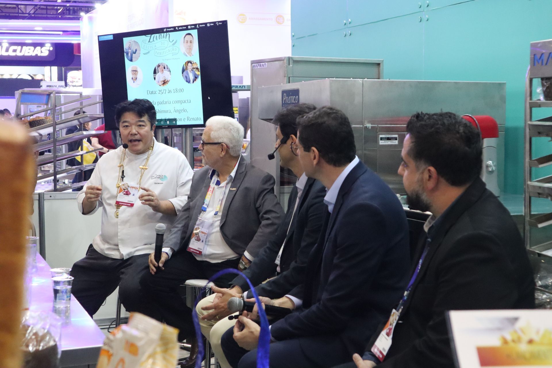 Um grupo de homens estão sentados ao redor de uma mesa conversando entre si.