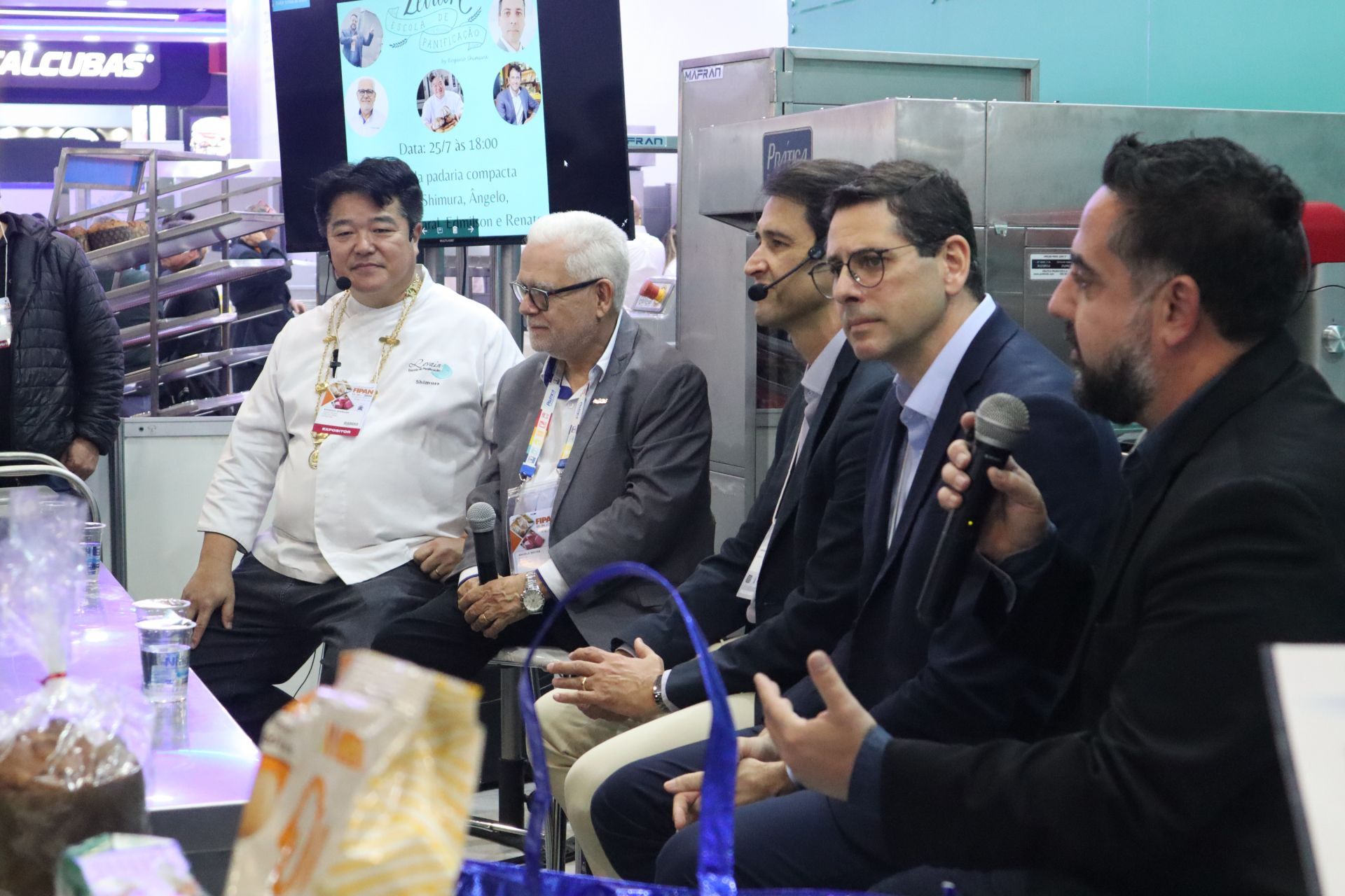 Um grupo de homens está sentado em uma fileira falando em microfones.