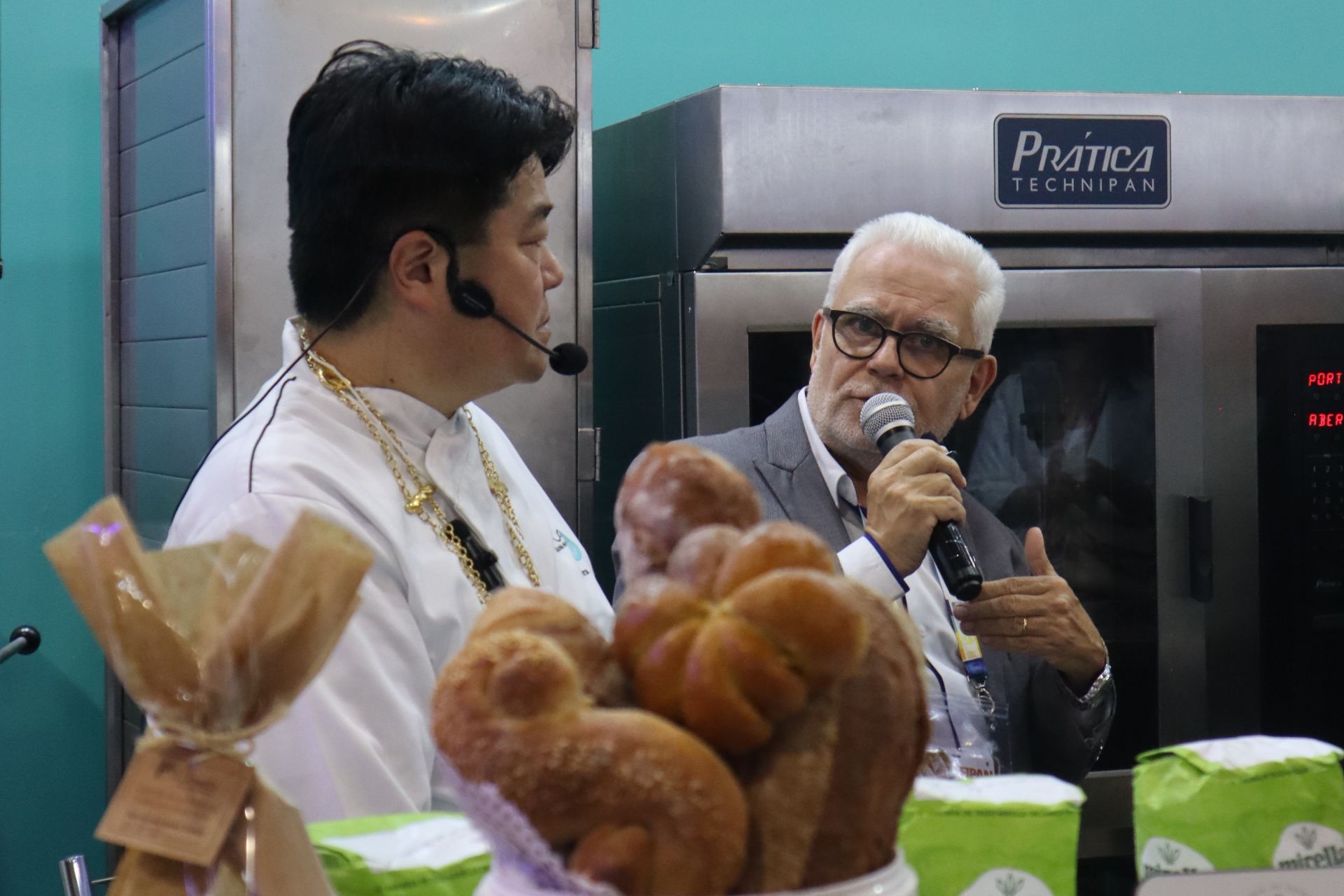 Um homem está falando em um microfone enquanto outro homem segura um monte de pão.