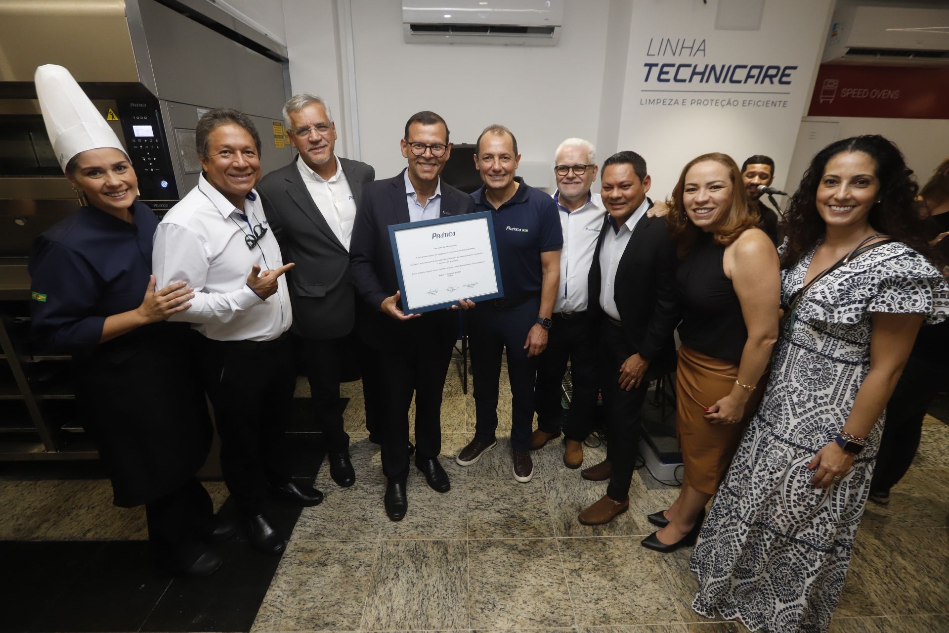 Grupo de pessoas segurando um documento emoldurado em uma sala com uma placa.