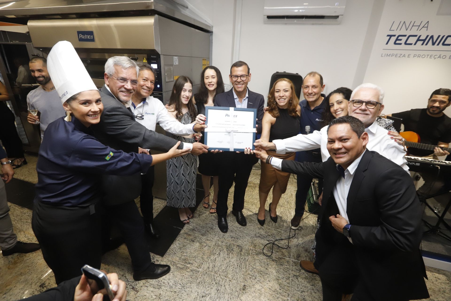 Grupo de pessoas segurando um certificado, comemorando em uma cozinha moderna.