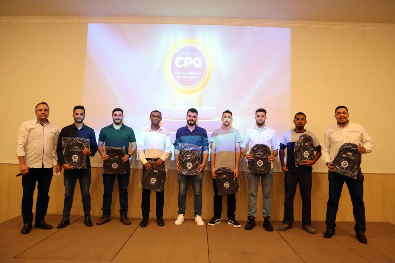 Um grupo de homens está em frente a uma tela de projetor segurando troféus.