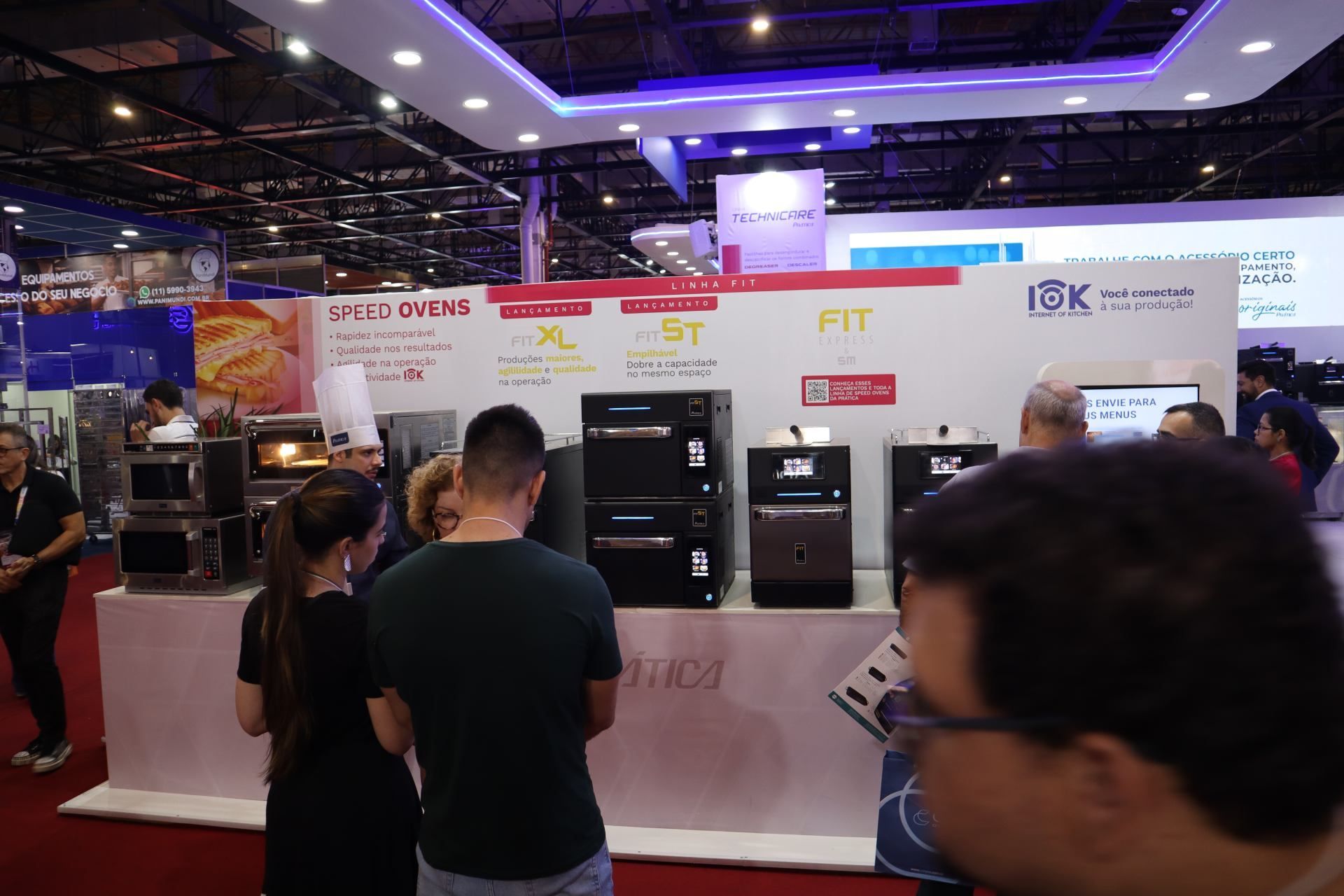Um grupo de pessoas está em uma sala olhando para uma exposição de eletrodomésticos.