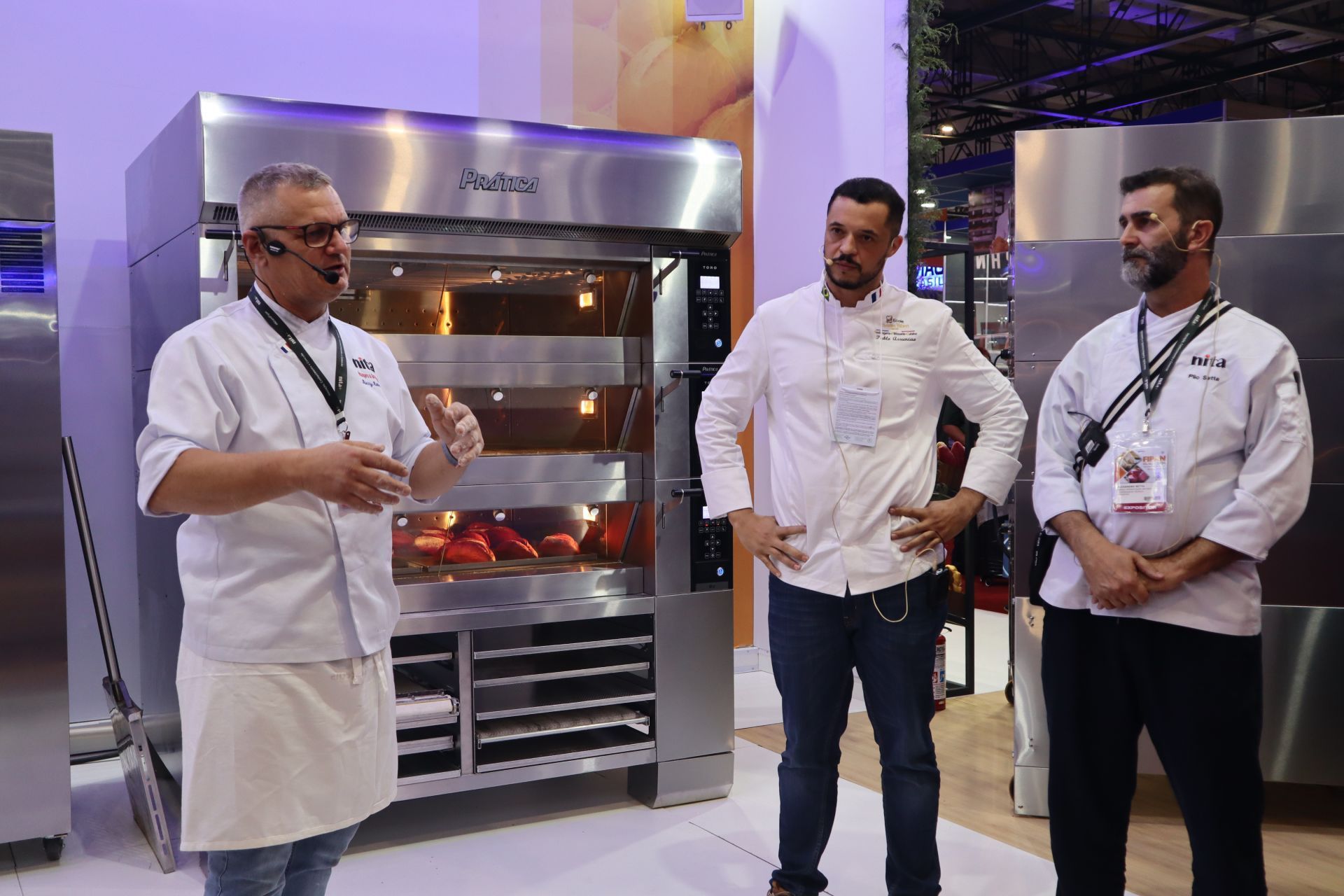 Três homens estão diante de um forno de aço inoxidável.