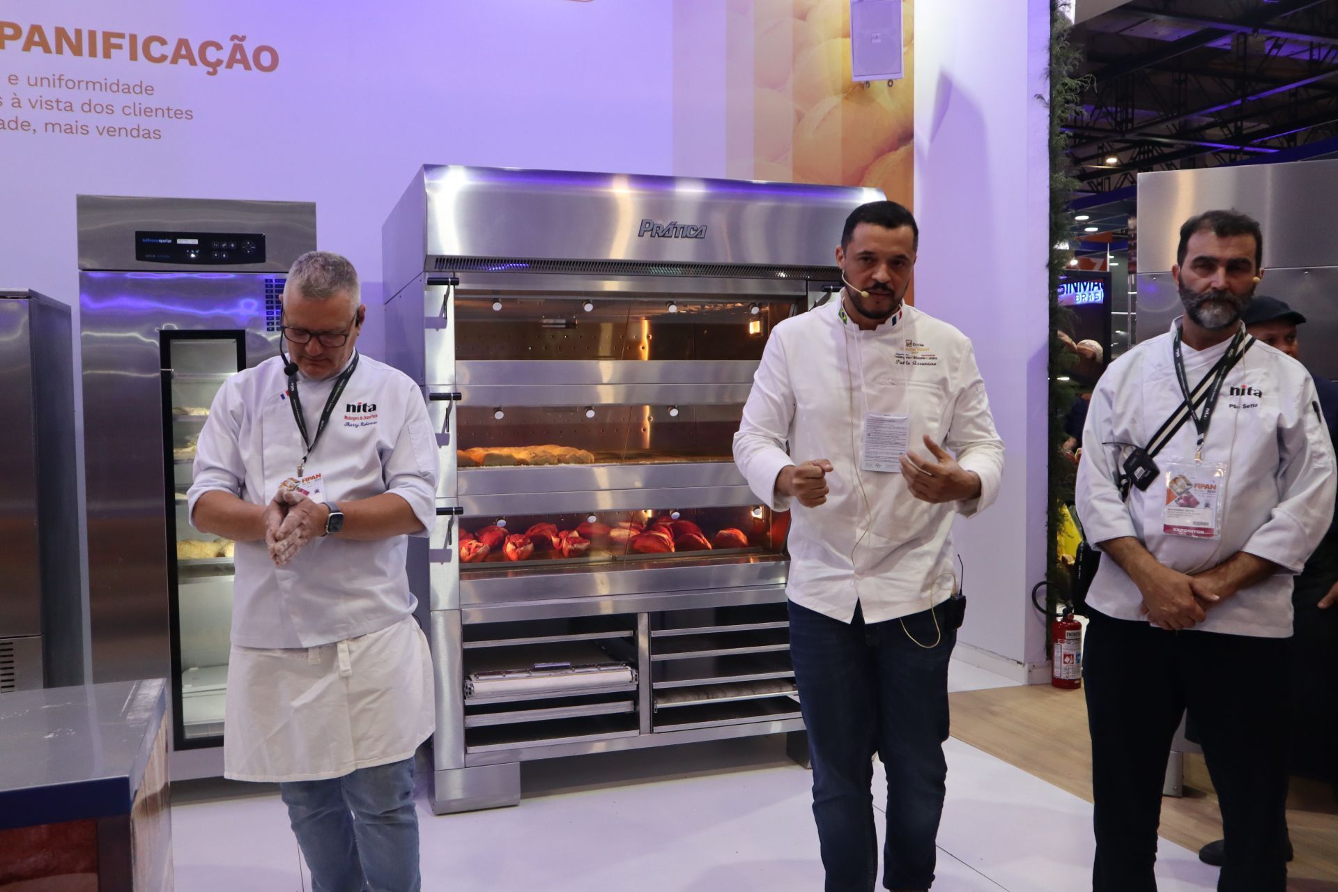 Três homens estão diante de um forno de aço inoxidável.