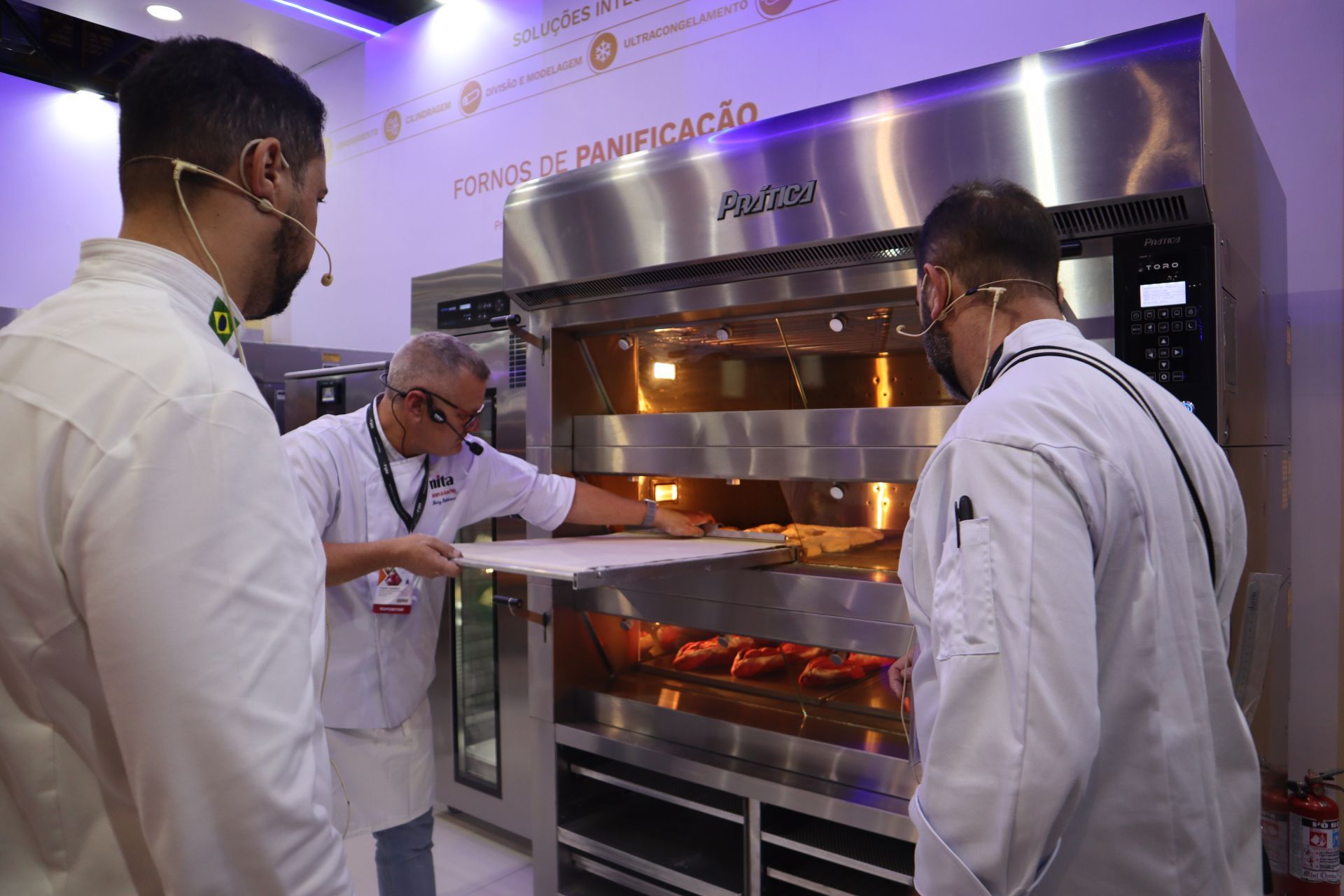 Um grupo de homens está em volta de um forno de aço inoxidável.