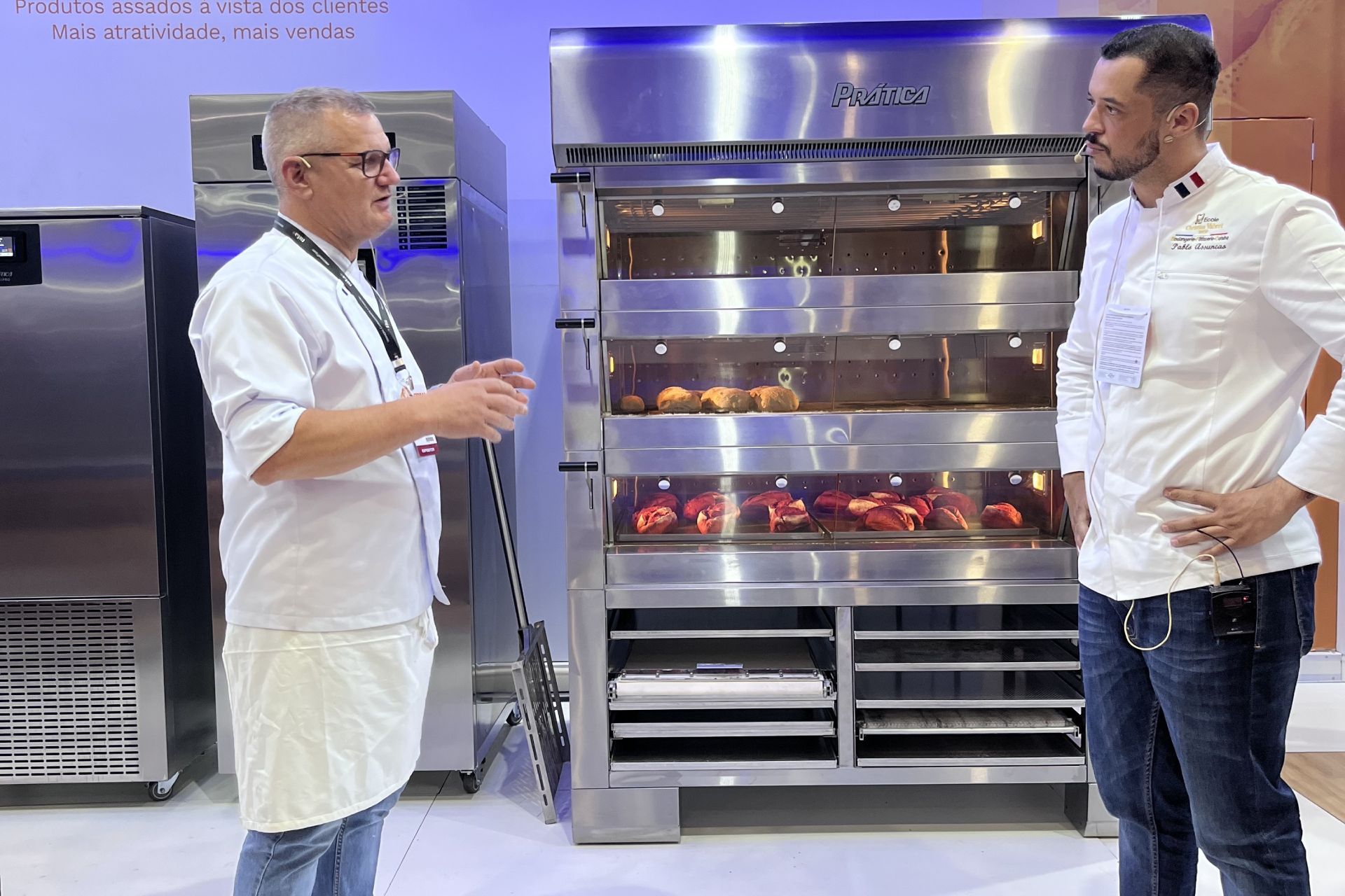 Dois homens estão diante de um forno de aço inoxidável.