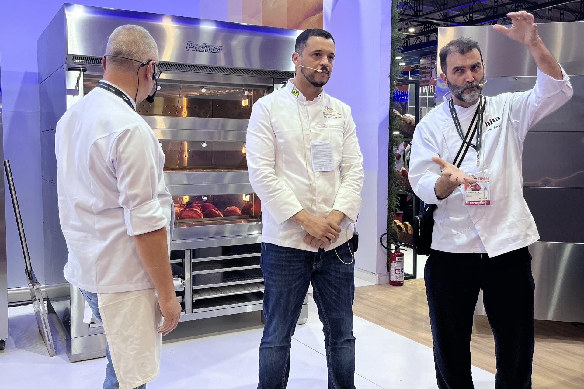 Três homens estão diante de um forno de aço inoxidável.