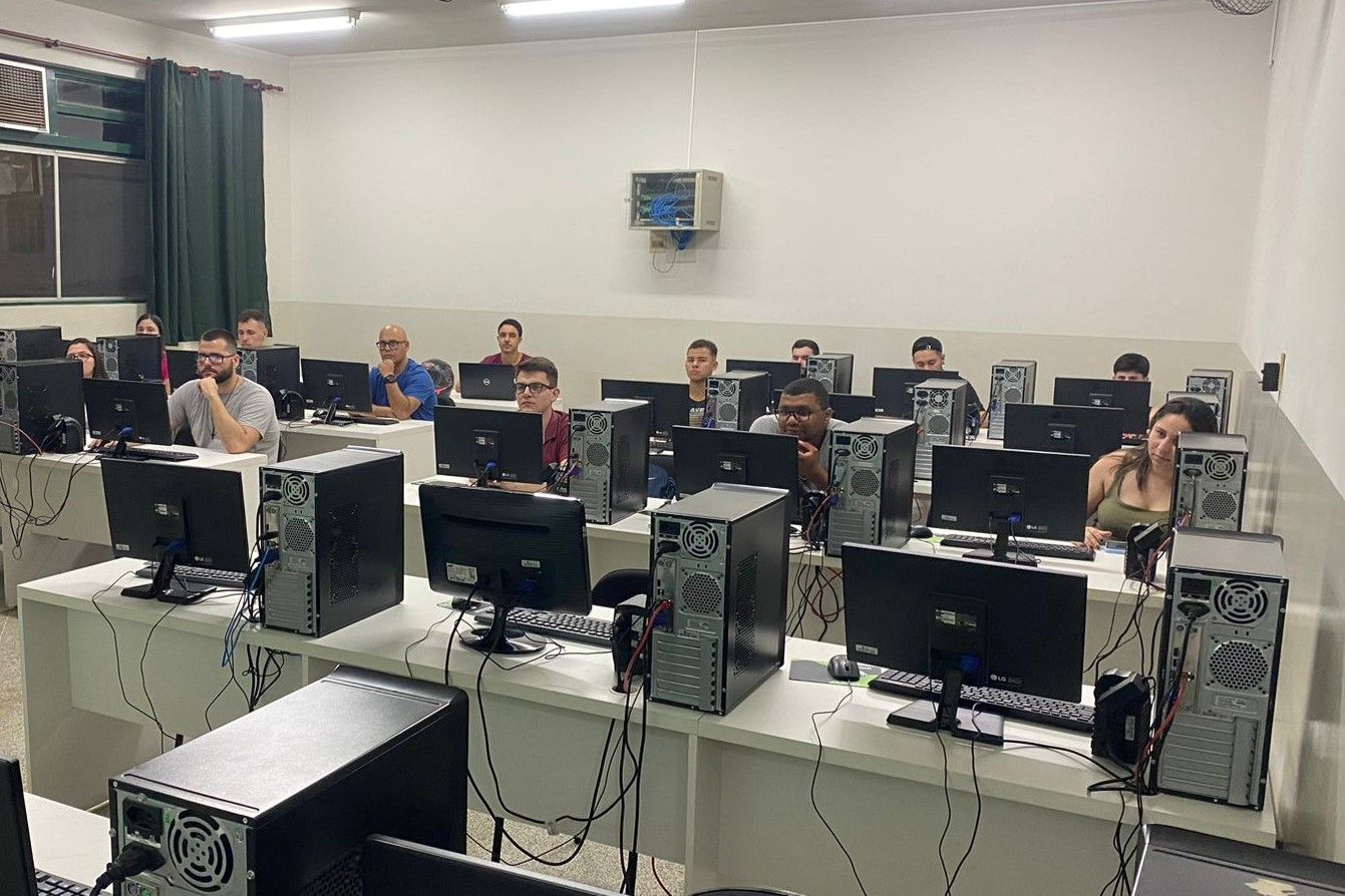 Um grupo de pessoas está sentado em mesas em um laboratório de informática.