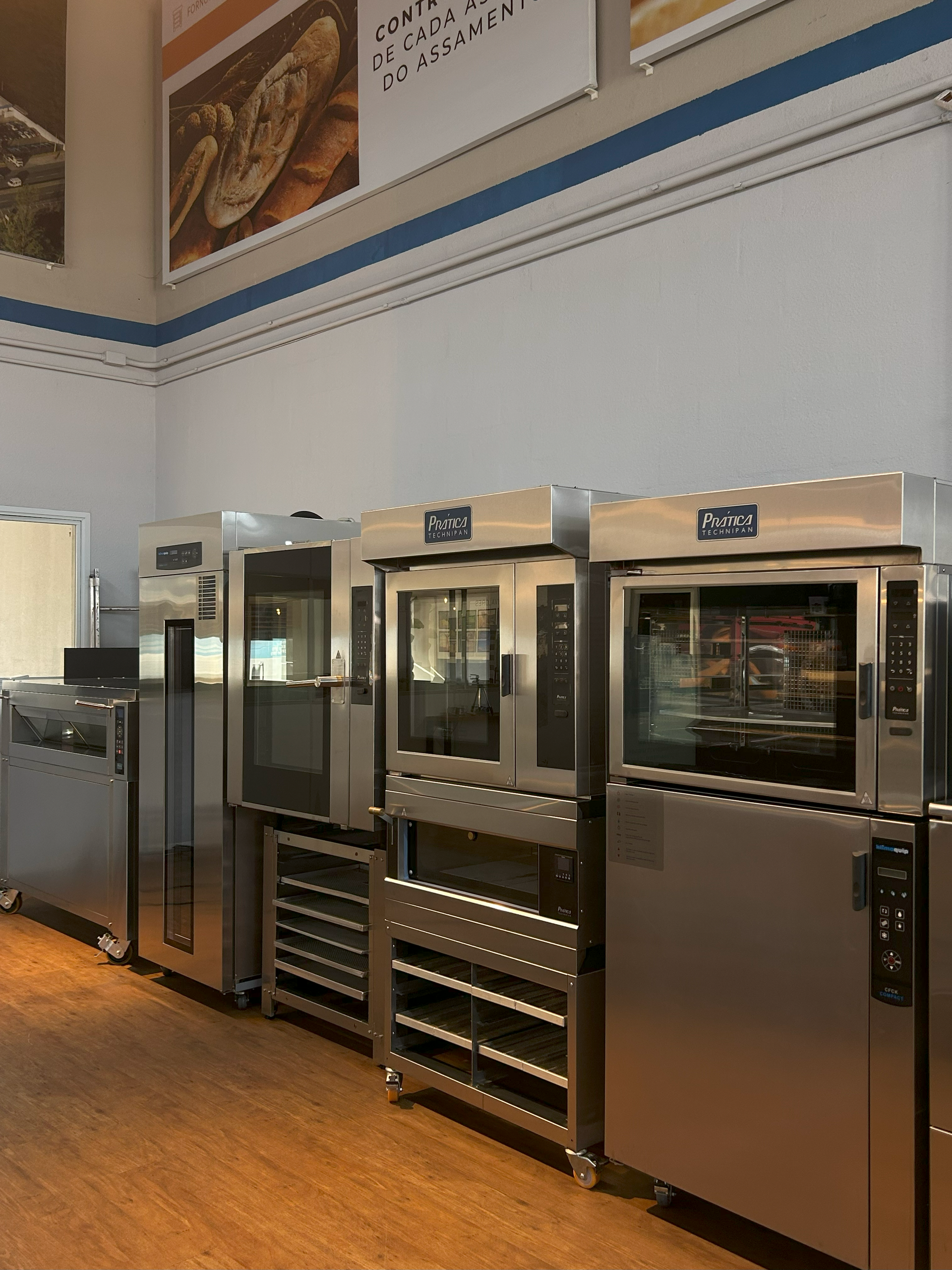 Uma fileira de fornos de aço inoxidável estão alinhados em uma cozinha