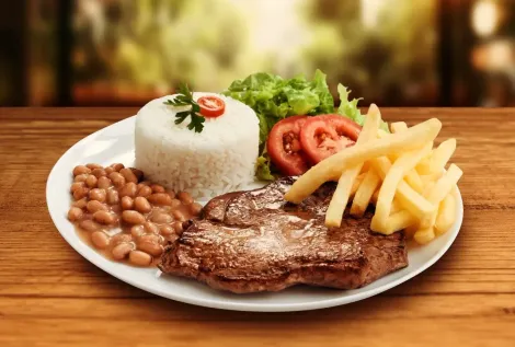 Prato de bife, arroz, feijão, batatas fritas, salada e tomates em uma mesa de madeira.