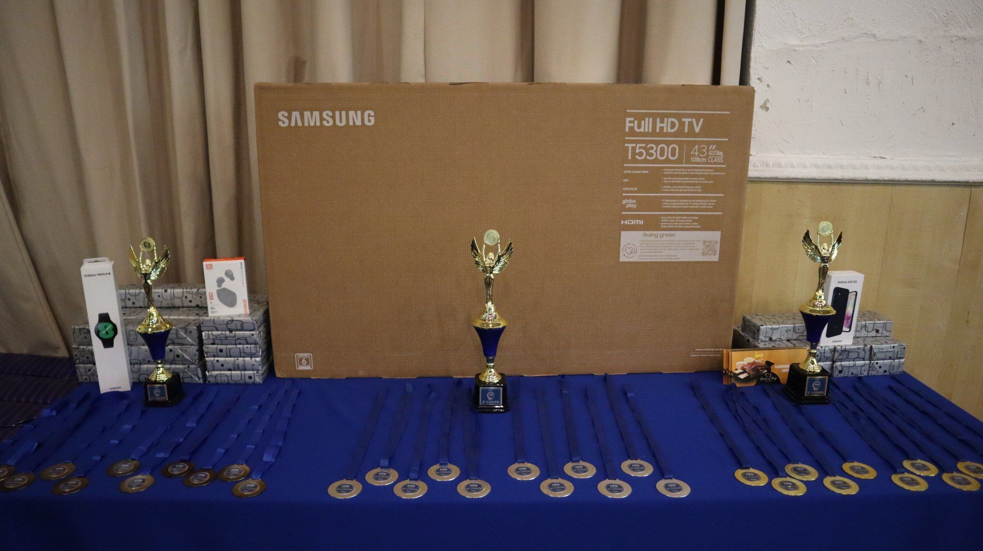 Uma mesa com troféus, medalhas e uma TV Samsung.