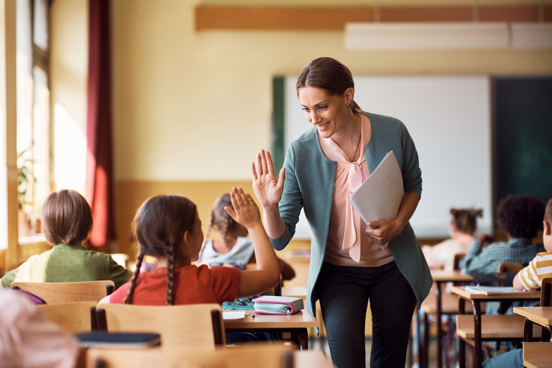 A teacher is giving a high five to a student in a classroom.