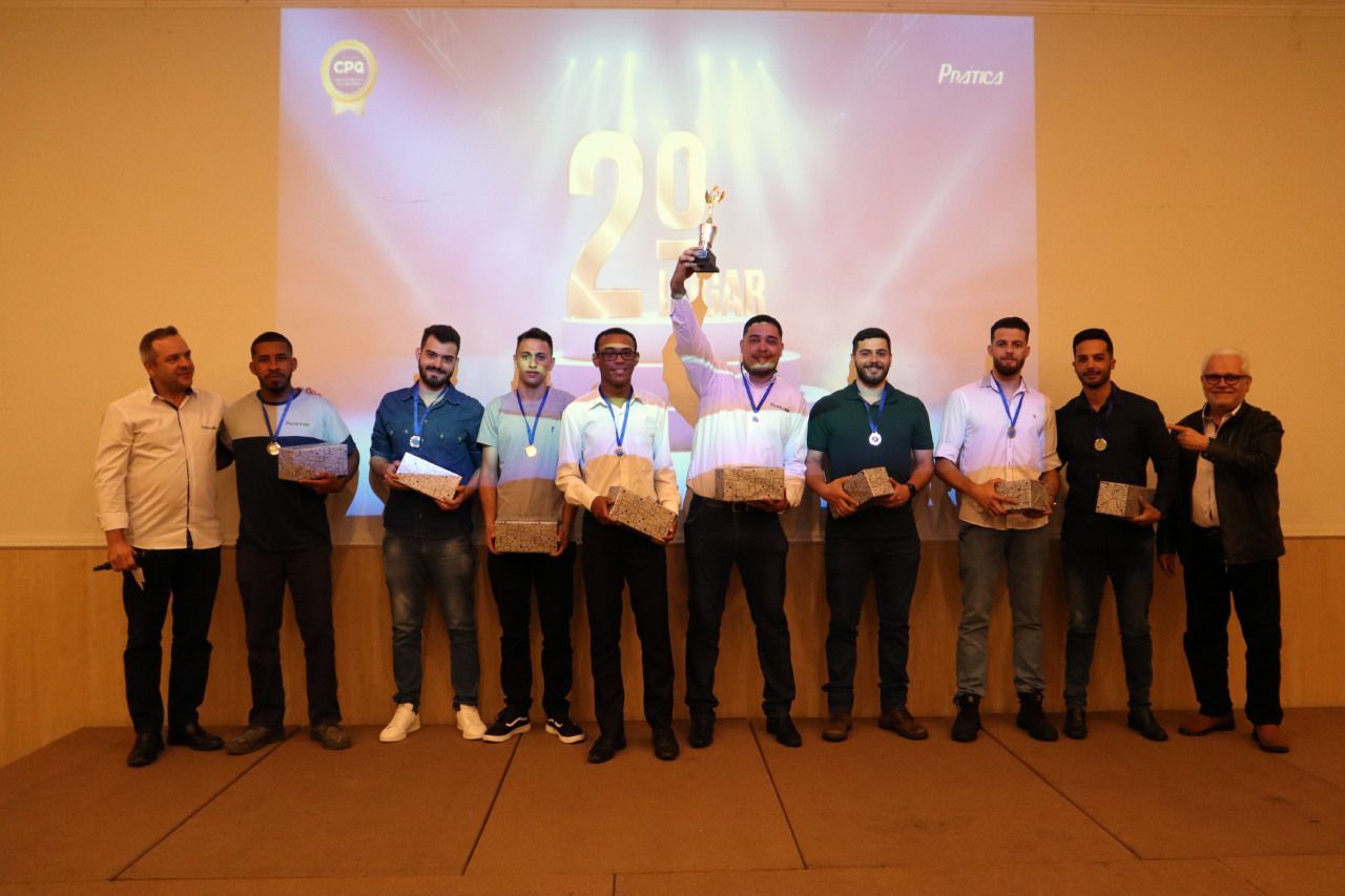 Um grupo de homens está em pé em frente a uma tela grande segurando troféus.