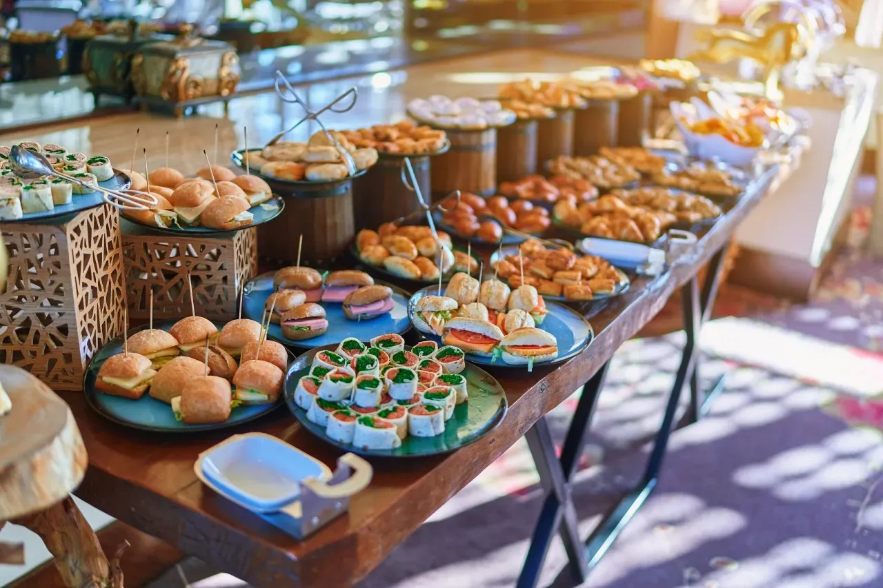 Mesa de buffet com diversos aperitivos, incluindo mini-hambúrgueres e mini-sanduíches.