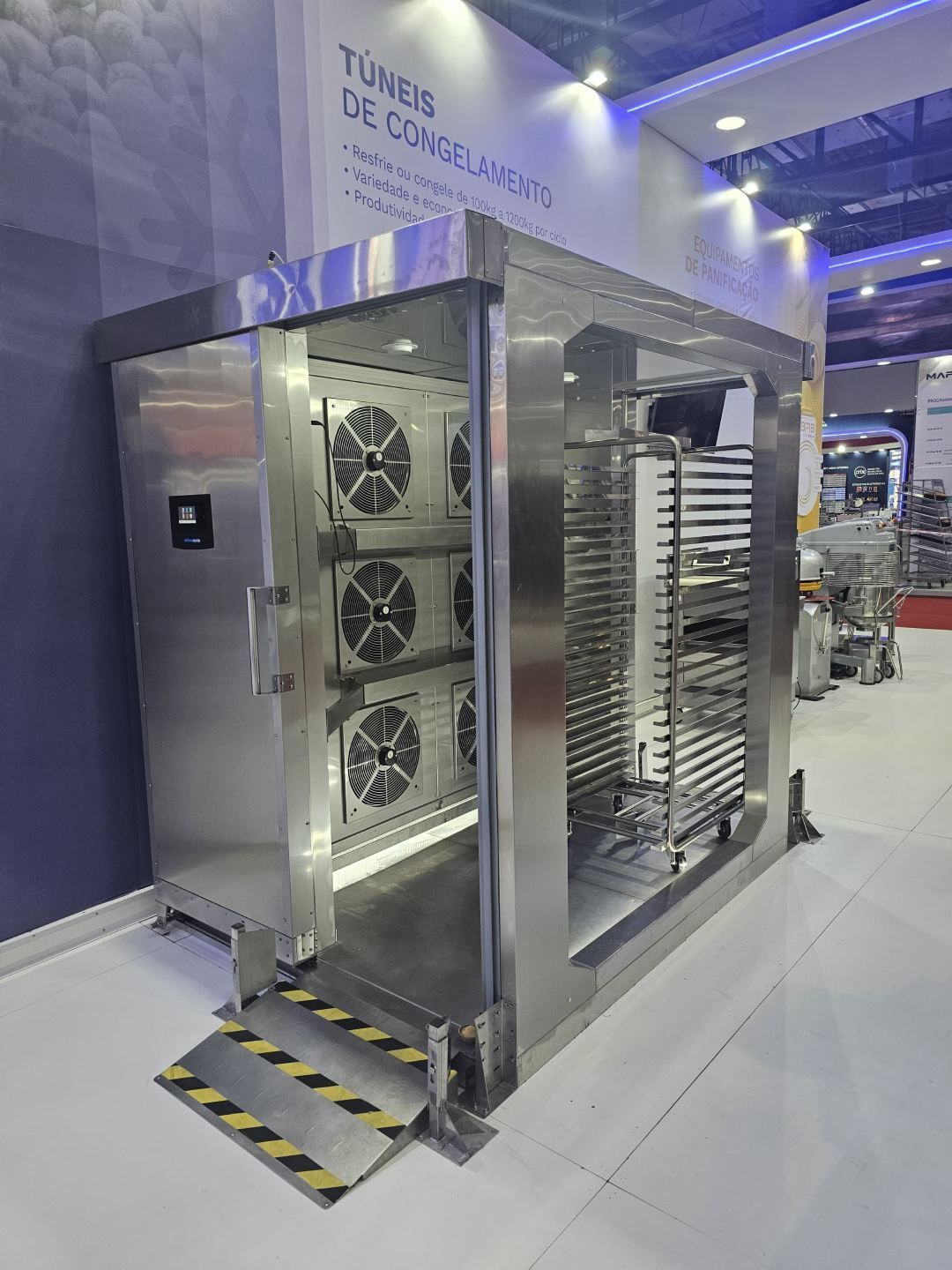 Uma grande geladeira de aço inoxidável está sobre um piso branco.