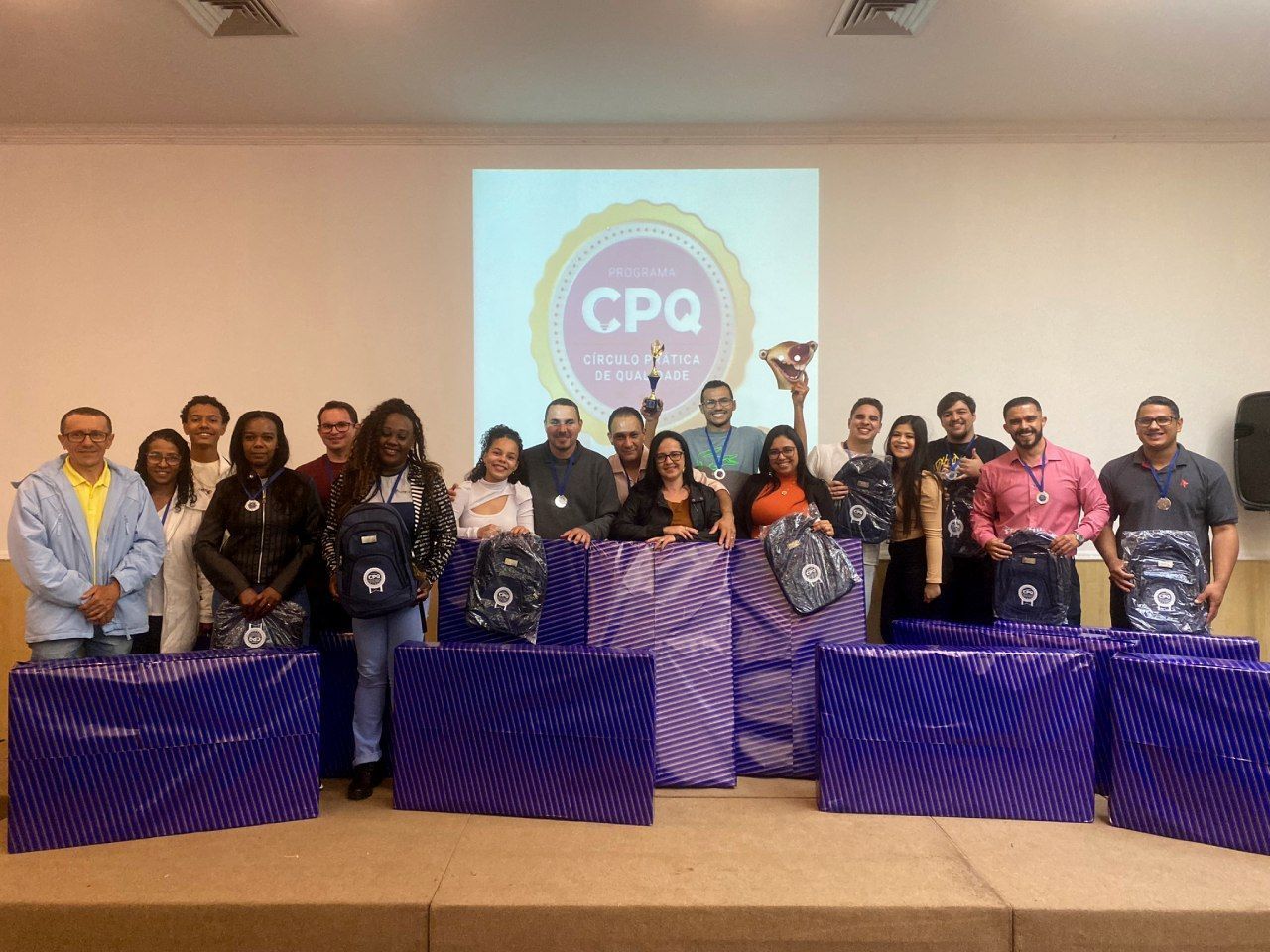 Um grupo de pessoas está posando para uma foto em frente a uma tela de projetor.