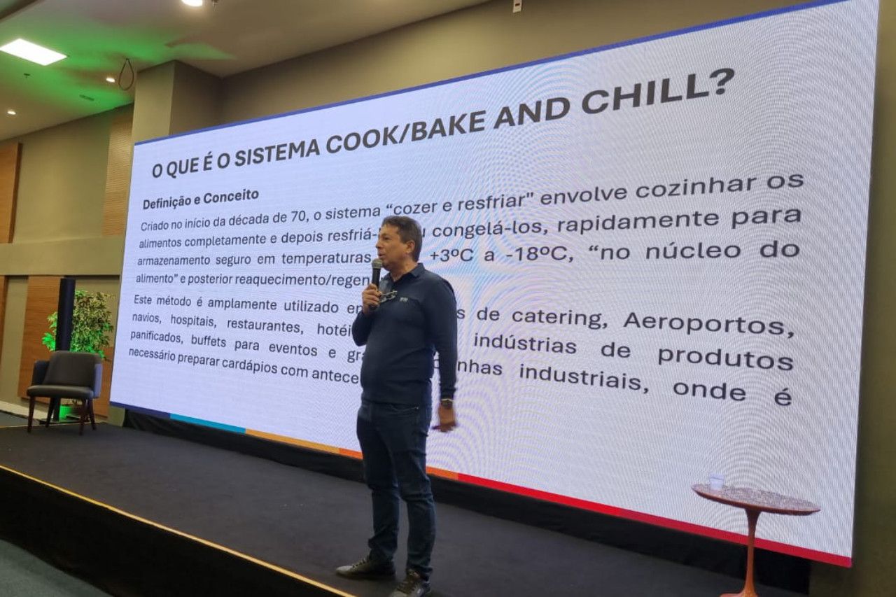 Um homem está em pé na frente de uma tela grande falando em um microfone.