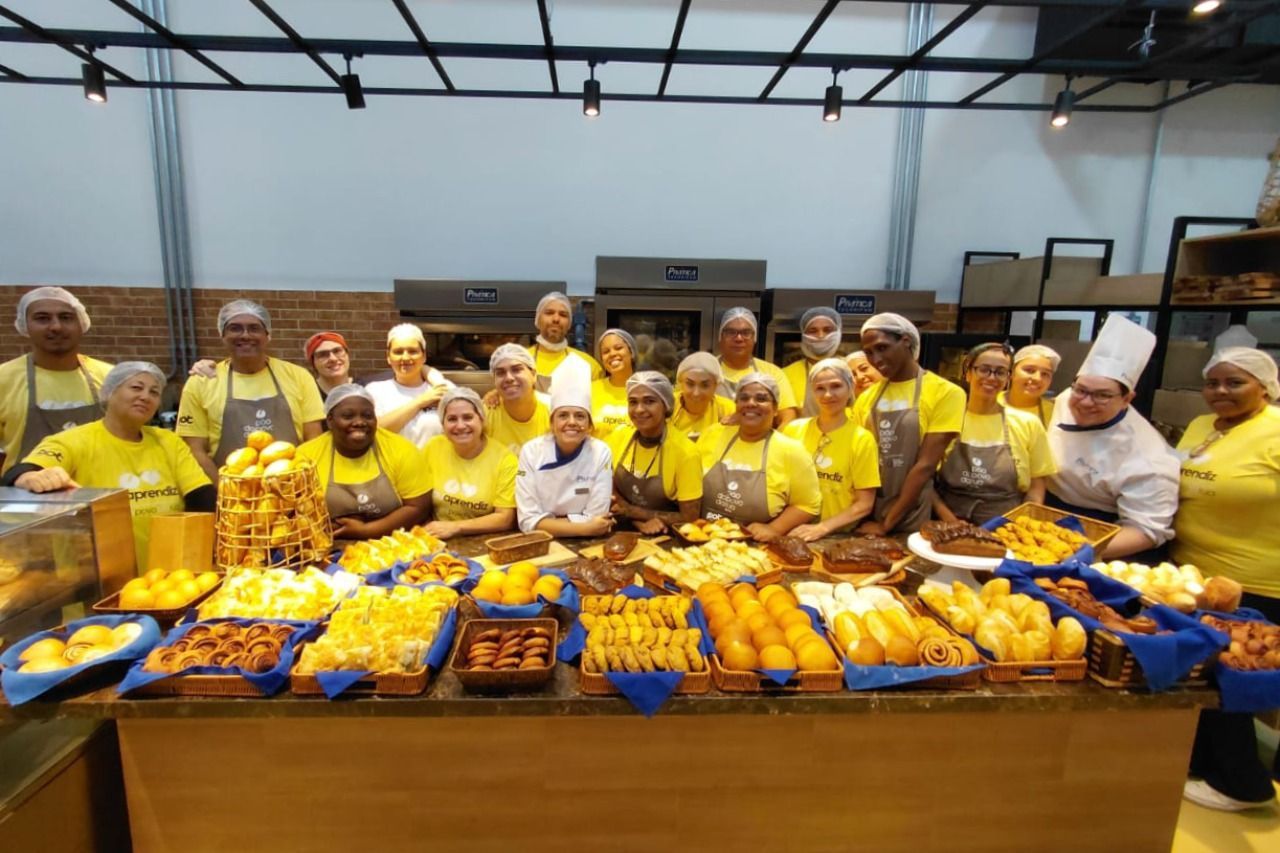 Um grupo de pessoas vestindo camisas e aventais amarelos está atrás de um balcão de produtos de panificação.