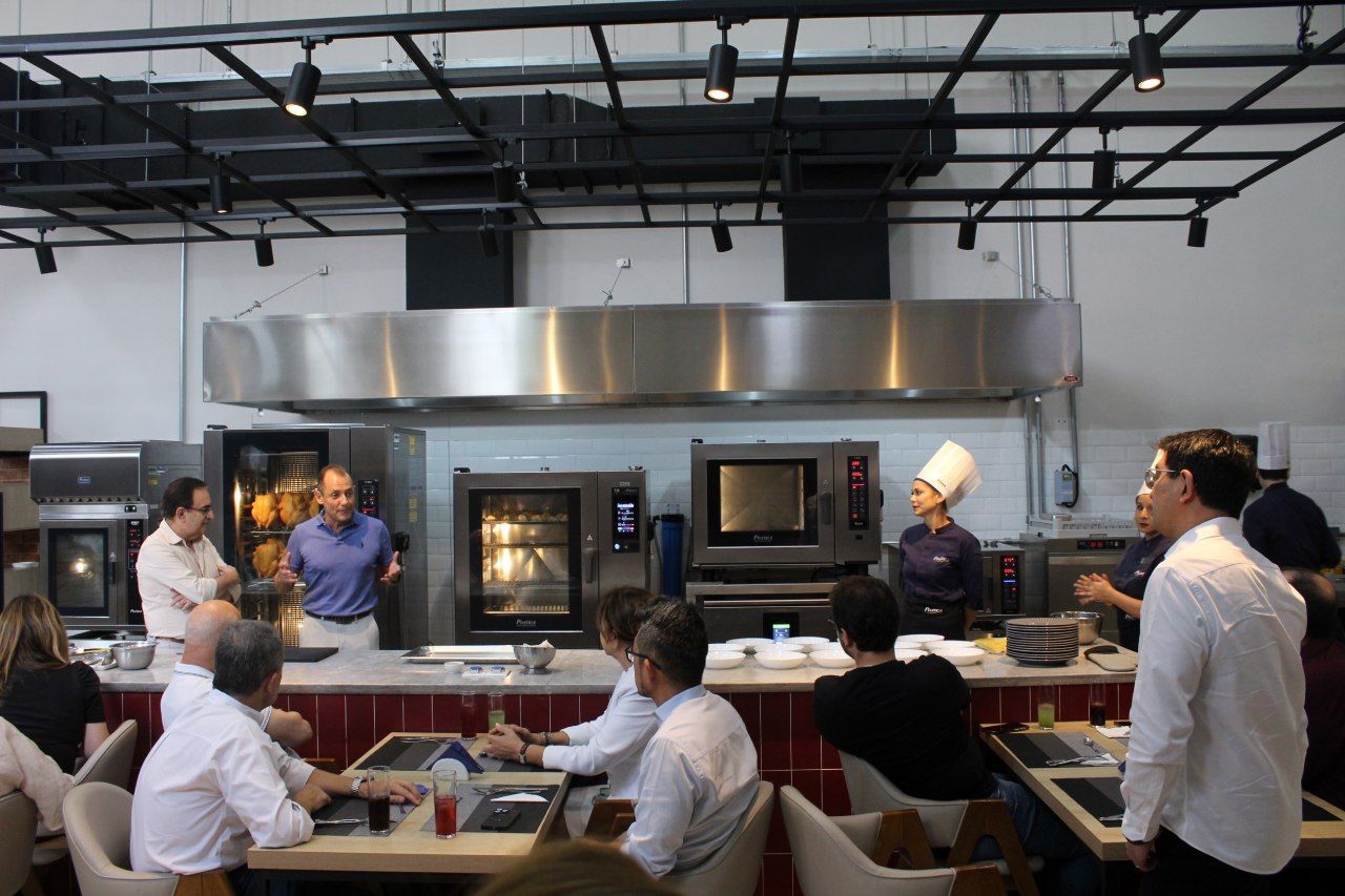 Um grupo de pessoas está sentado em mesas em uma cozinha.