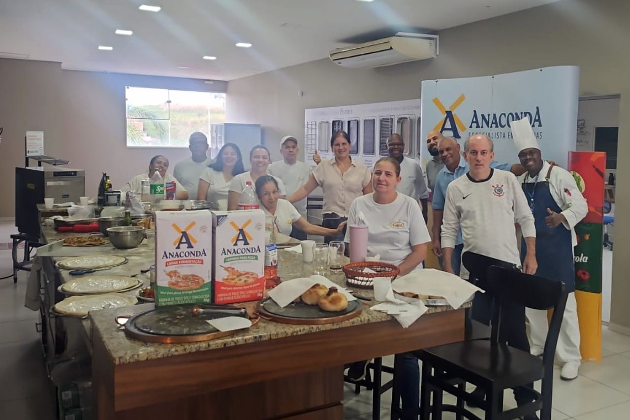 Um grupo de pessoas está em pé ao redor de uma mesa na cozinha.