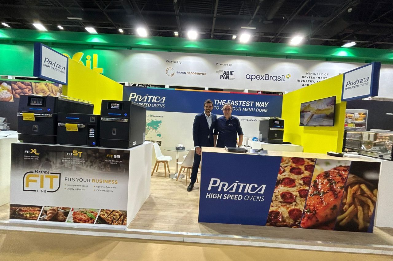 Dois homens estão parados em frente a uma barraca que diz prática