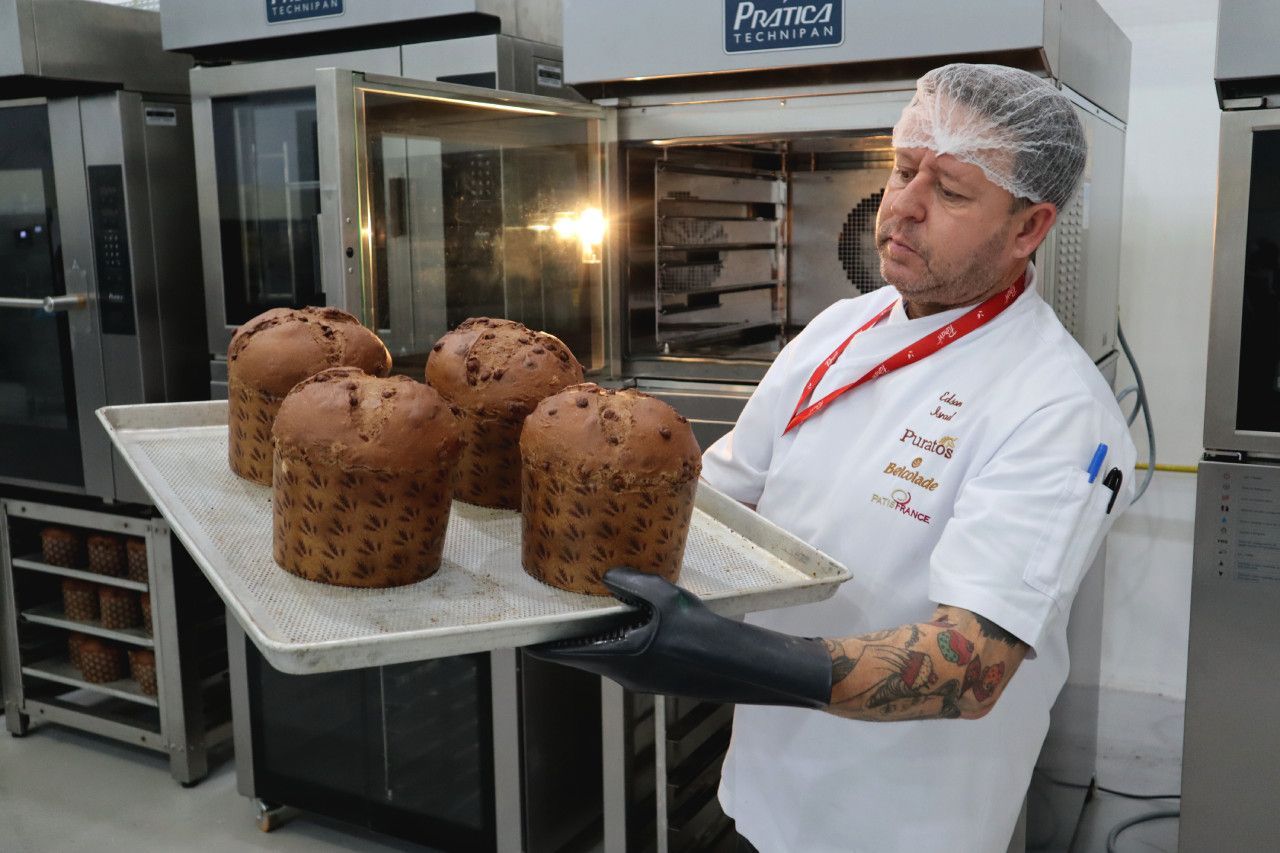 Um homem de camisa branca segura uma bandeja de pão