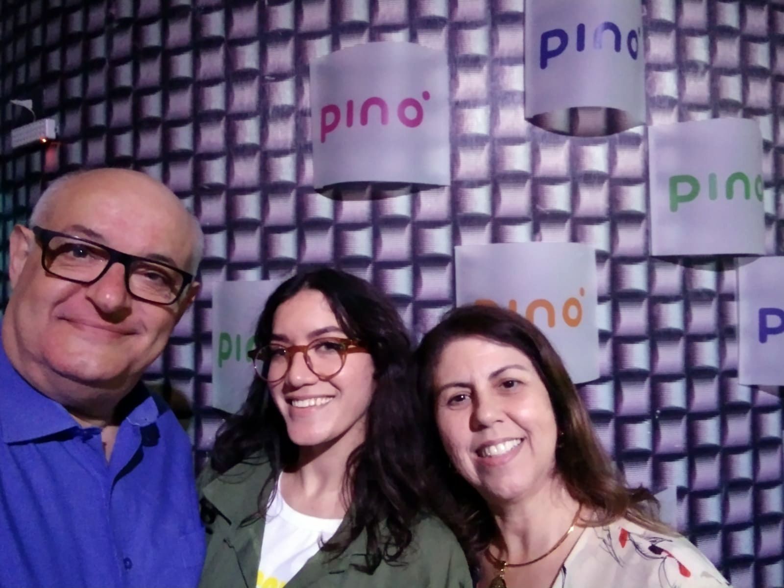 Um homem e duas mulheres estão posando para uma foto em frente a uma parede que diz pino