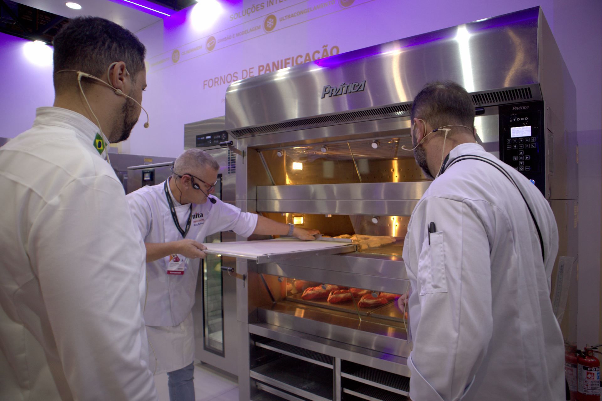 Um grupo de homens está em volta de um forno de aço inoxidável.