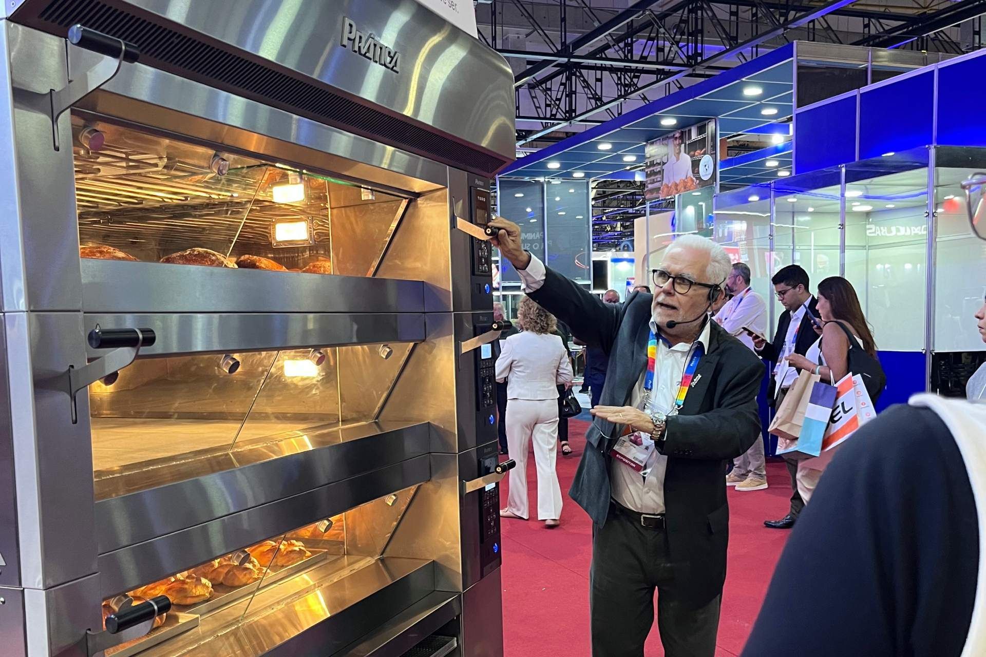 Um homem de terno aponta para um forno de aço inoxidável.