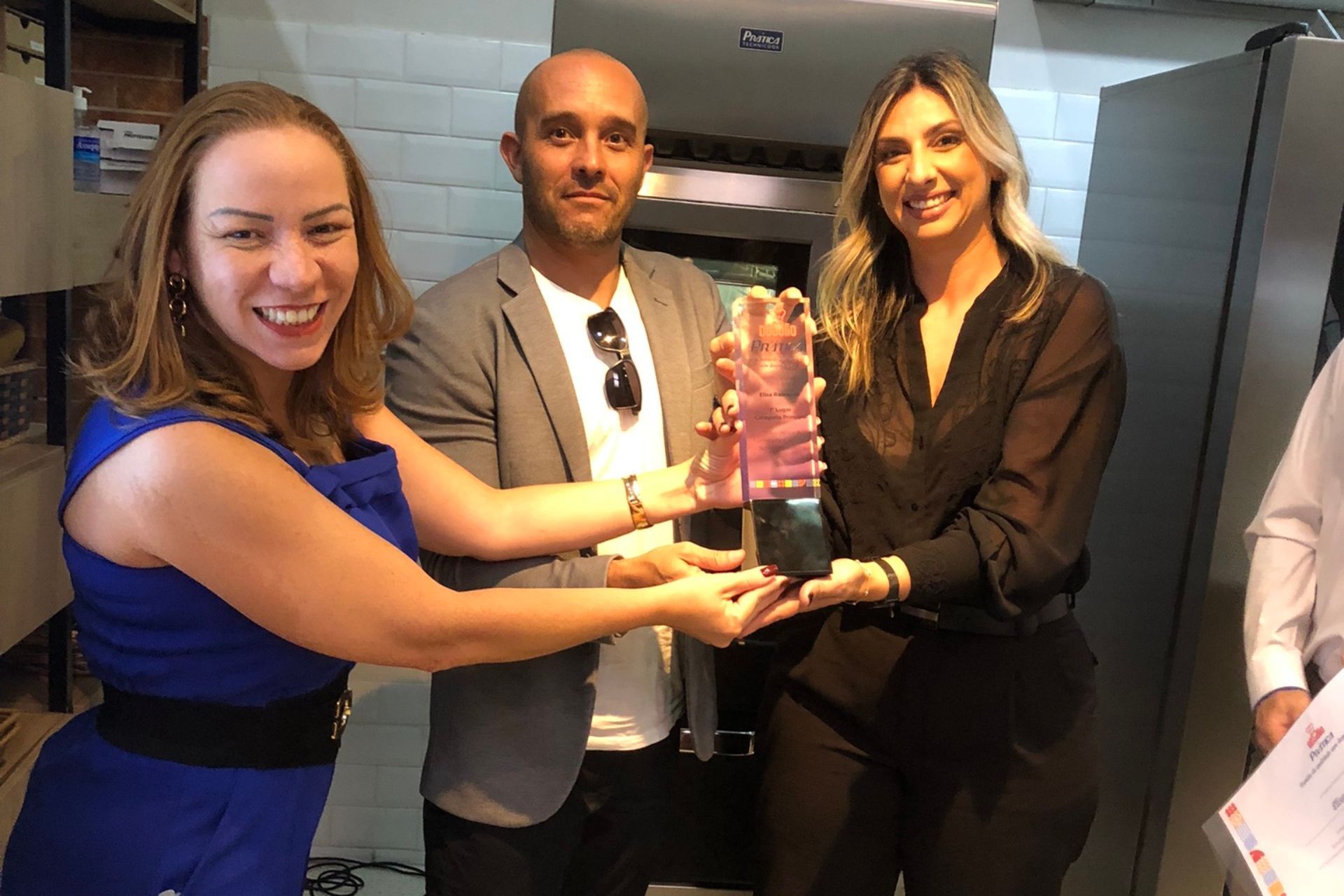 Três pessoas sorrindo enquanto recebem um prêmio