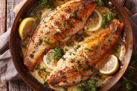 Filés de peixe truta assados ​​em uma frigideira rústica, guarnecidos com fatias de limão e ervas.