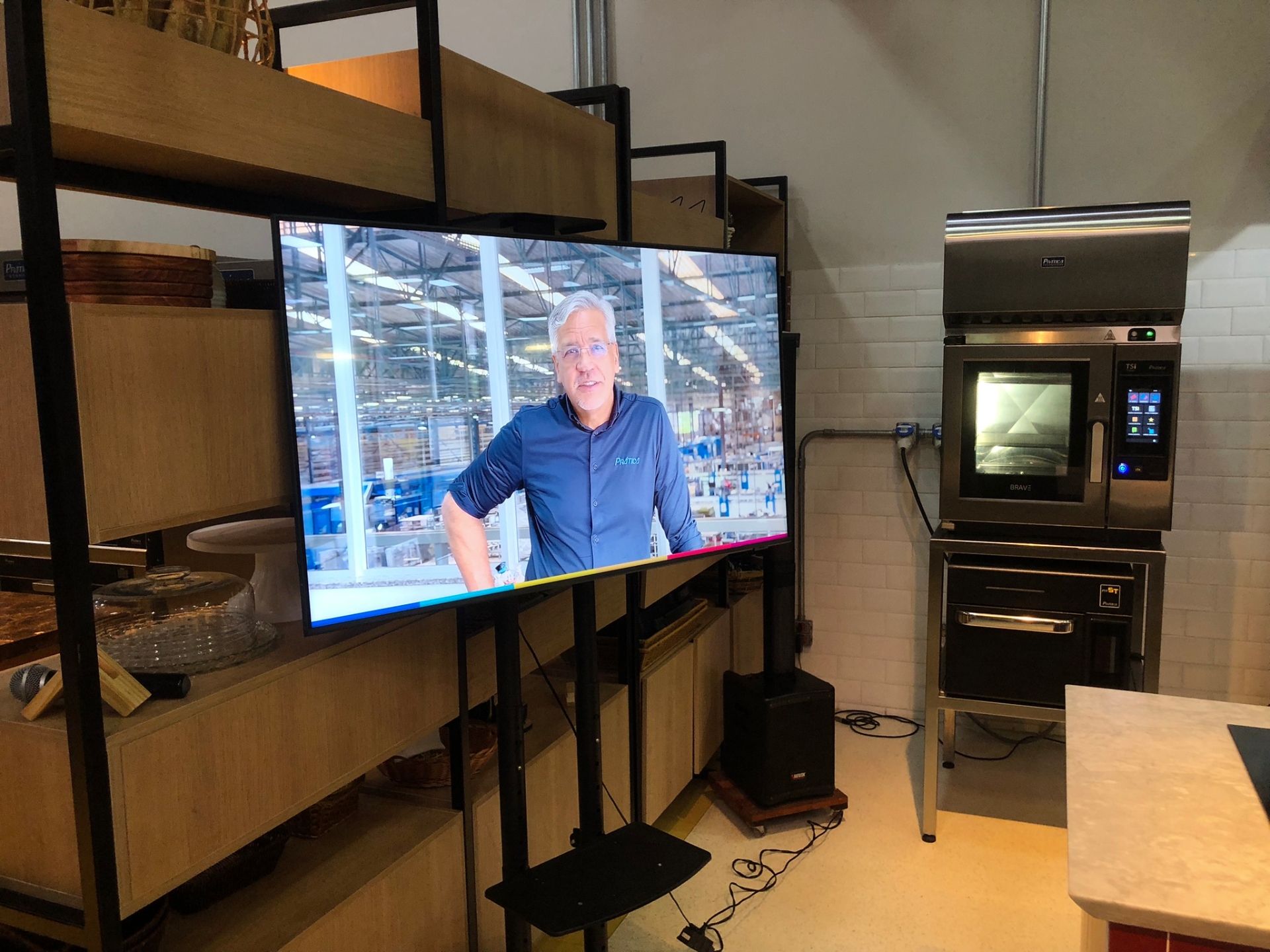 Homem na tela em frente a prateleiras e forno; um programa ou demonstração de culinária está acontecendo.