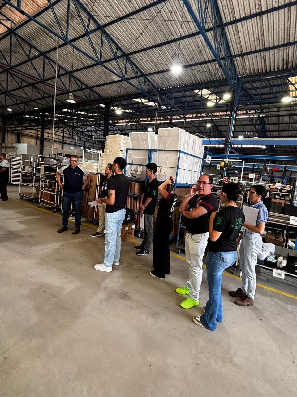 Grupo de pessoas em visita guiada a uma fábrica. O guia turístico está se dirigindo ao grupo em um ambiente de armazém.