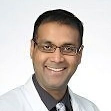 A man wearing glasses and a white coat is smiling for the camera.