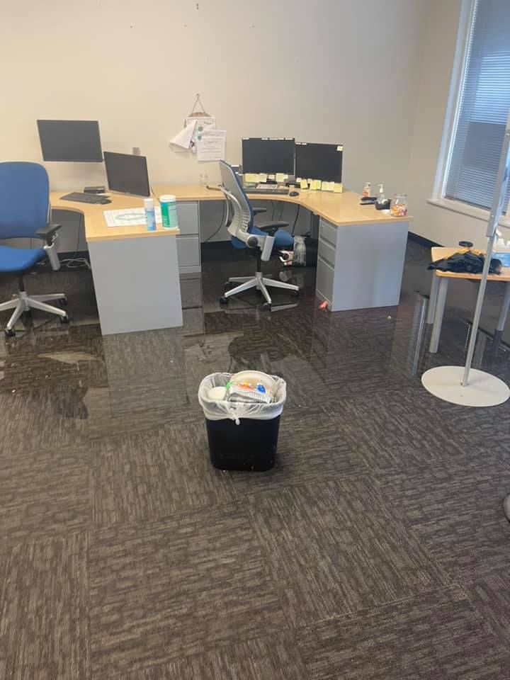 Office with water on the floor, desk, chairs, trash can in the middle.