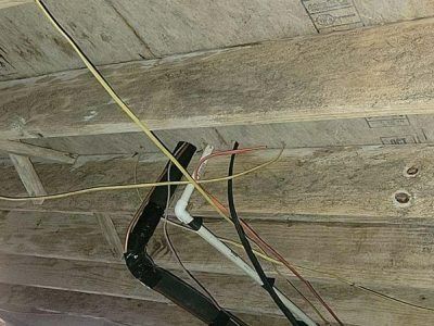 Electrical wiring and plumbing beneath wooden ceiling boards.
