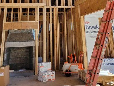 Interior of a building under construction, wooden framing, orange ladder, Tyvek wrap, boxes.