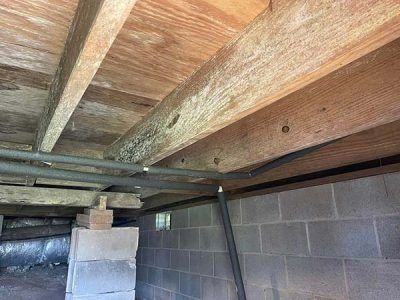 Wooden beams and subfloor above cinder block foundation, with pipes running through.
