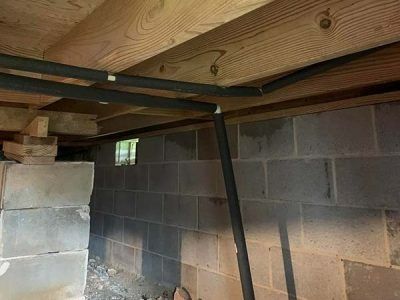 Black insulated pipes run through a dark basement with cinder block walls and wooden beams.