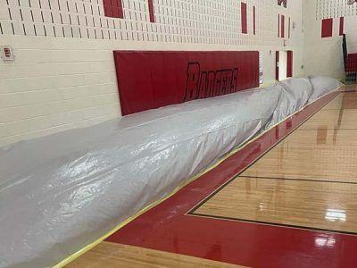 Long, gray padded wall covering along the side of a gymnasium floor, near a red padded wall.