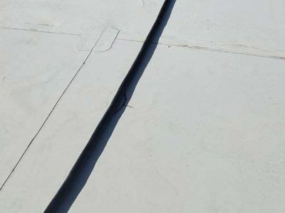 Dark seal along a concrete seam on a white surface, possibly a roof, with other cracks visible.