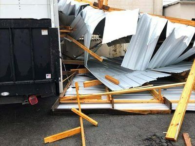 Damaged shed with collapsed metal roof next to a black truck. Wooden beams scattered.