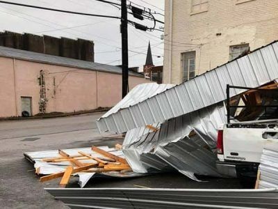 Damaged metal roofing debris on the ground and a truck, next to a building. Cloudy day.
